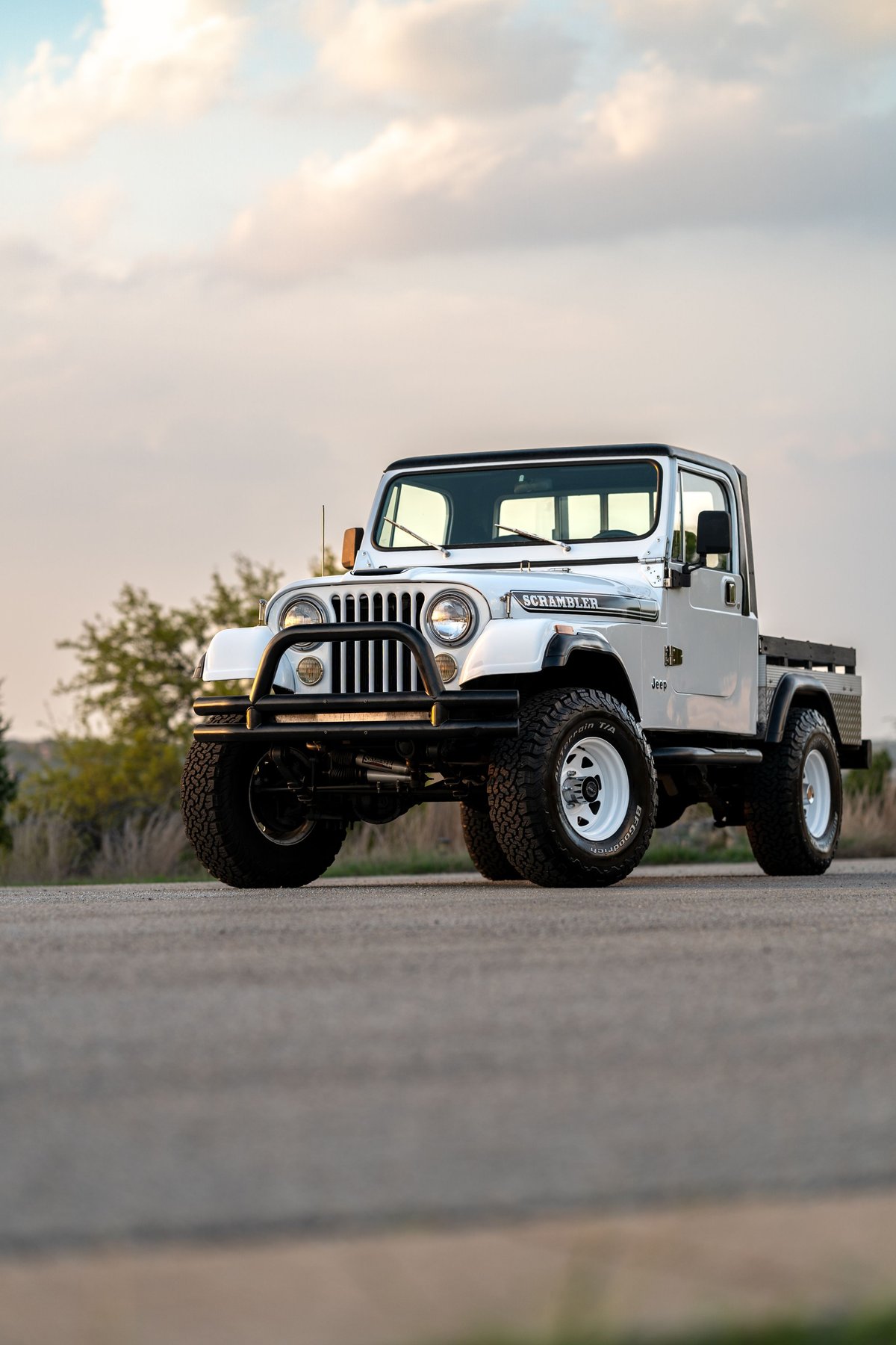 A white 1983 Jeep CJ-8 Scrambler pickup truck with black trim and white rims.