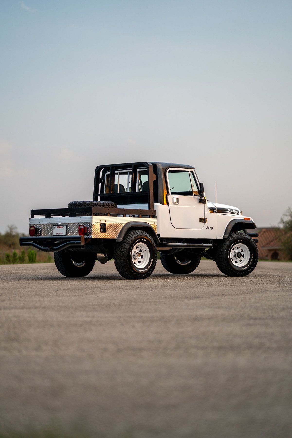 White 1983 Jeep CJ8 Scrambler with a flatbed conversion, roll cage, and white rims.