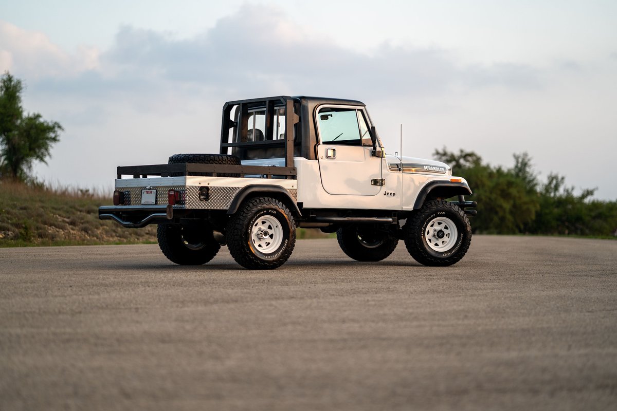 White 1983 Jeep Scrambler CJ-8 with custom flatbed, diamond plate trim, and white rims.