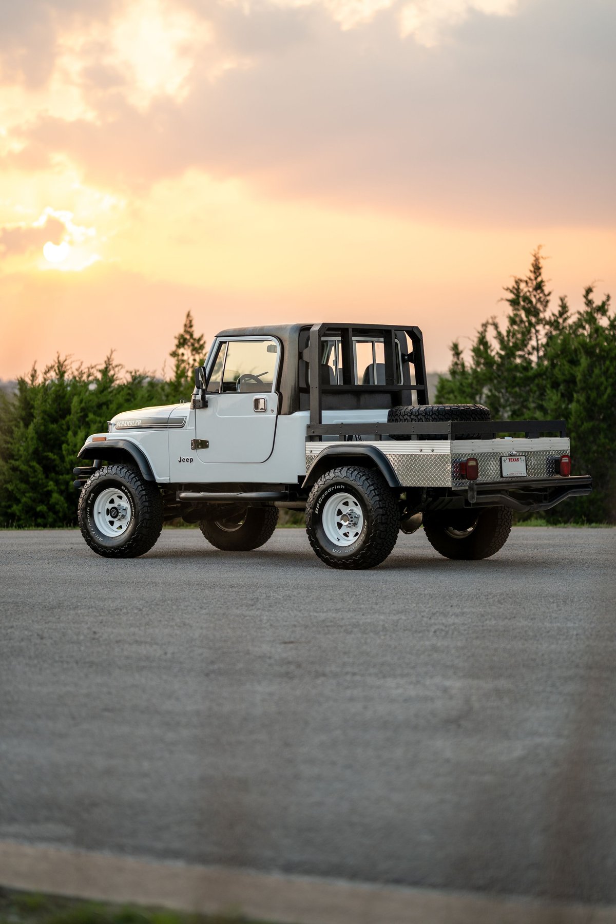 White 1983 Jeep Scrambler with a flatbed conversion, white rims, and off-road tires.