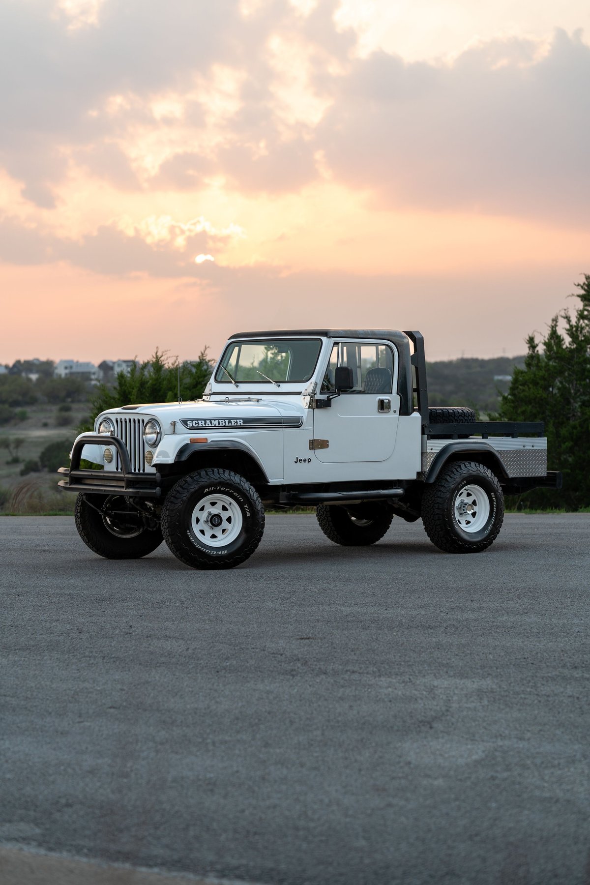White 1983 Jeep Scrambler CJ8 pickup with off-road tires, white rims, and black trim.
