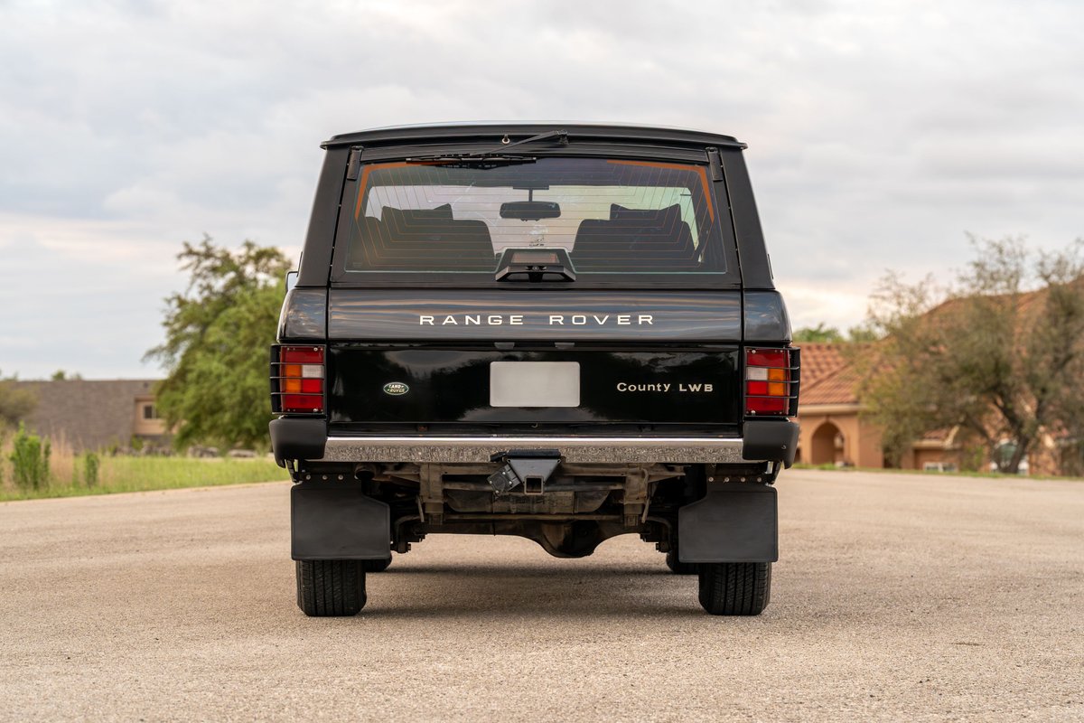 Rear view of a black 1994 Land Rover Range Rover County LWB with mud flaps and a tow hitch.