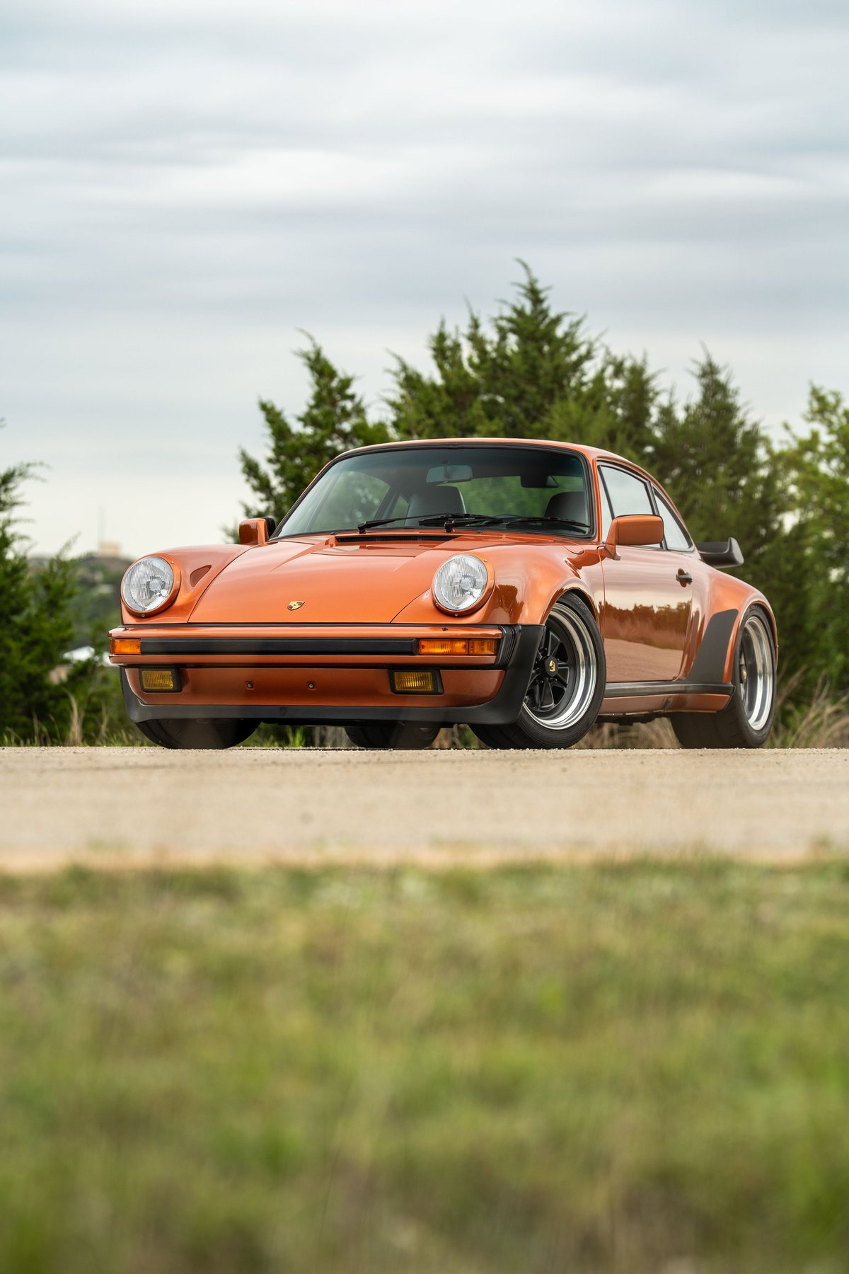 Front view of an orange metallic 1986 Porsche 930 Turbo coupe with black trim and Fuchs rims.