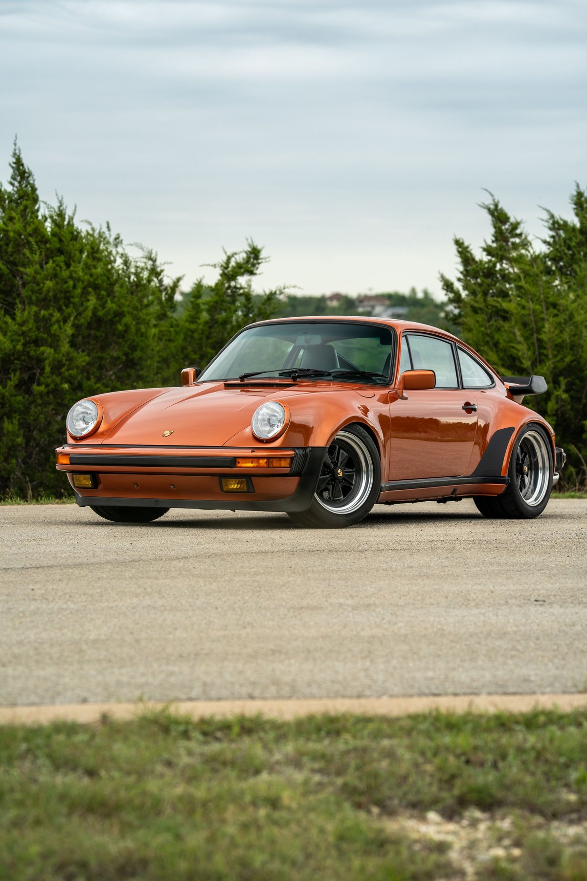 Orange metallic 1986 Porsche 930 Turbo with wide body kit and black Fuchs rims.