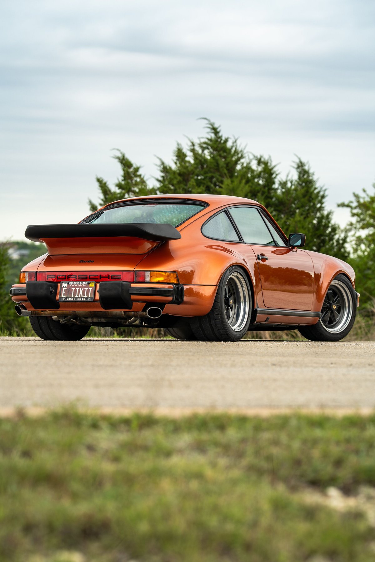 Rear view of a metallic orange 1986 Porsche 930 Turbo with a black whale tail spoiler.