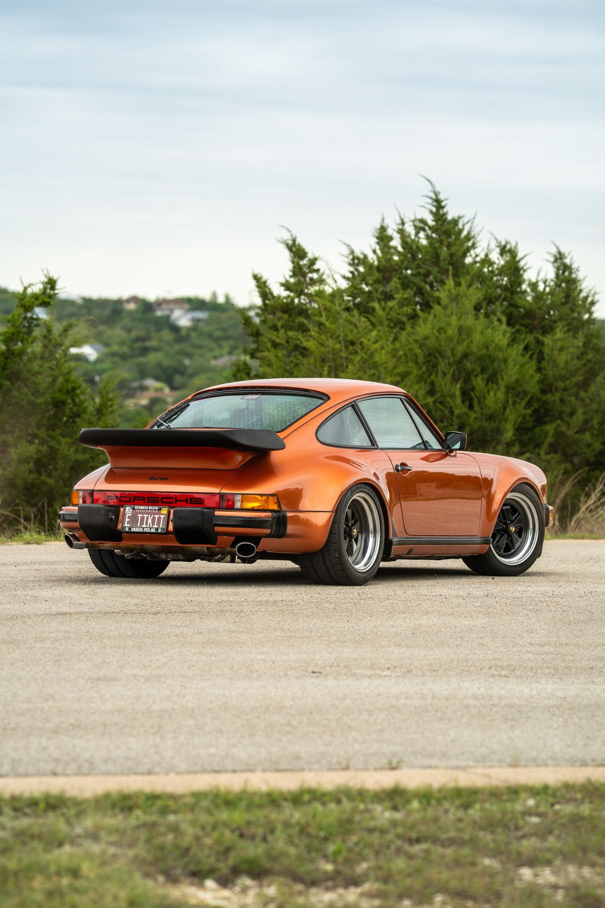 Rear view of a metallic orange 1986 Porsche 930 Turbo with a black whale tail spoiler and deep dish rims.