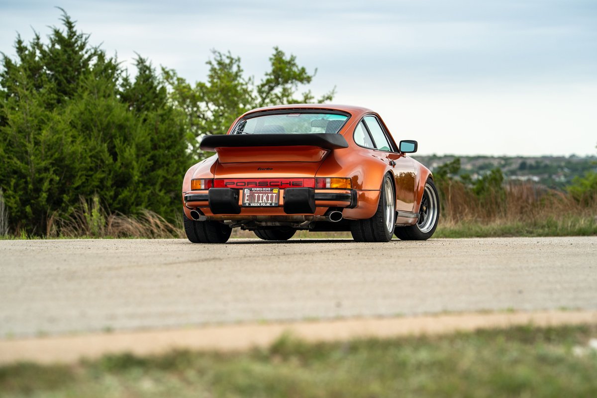 Rear view of an orange metallic 1986 Porsche 930 Turbo with a whale tail spoiler and Fuchs rims.