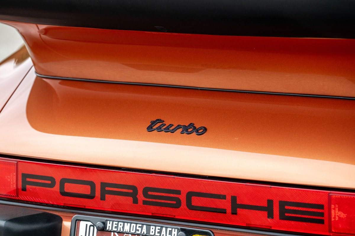 Close-up of an orange metallic 1986 Porsche 930 Turbo rear badging.