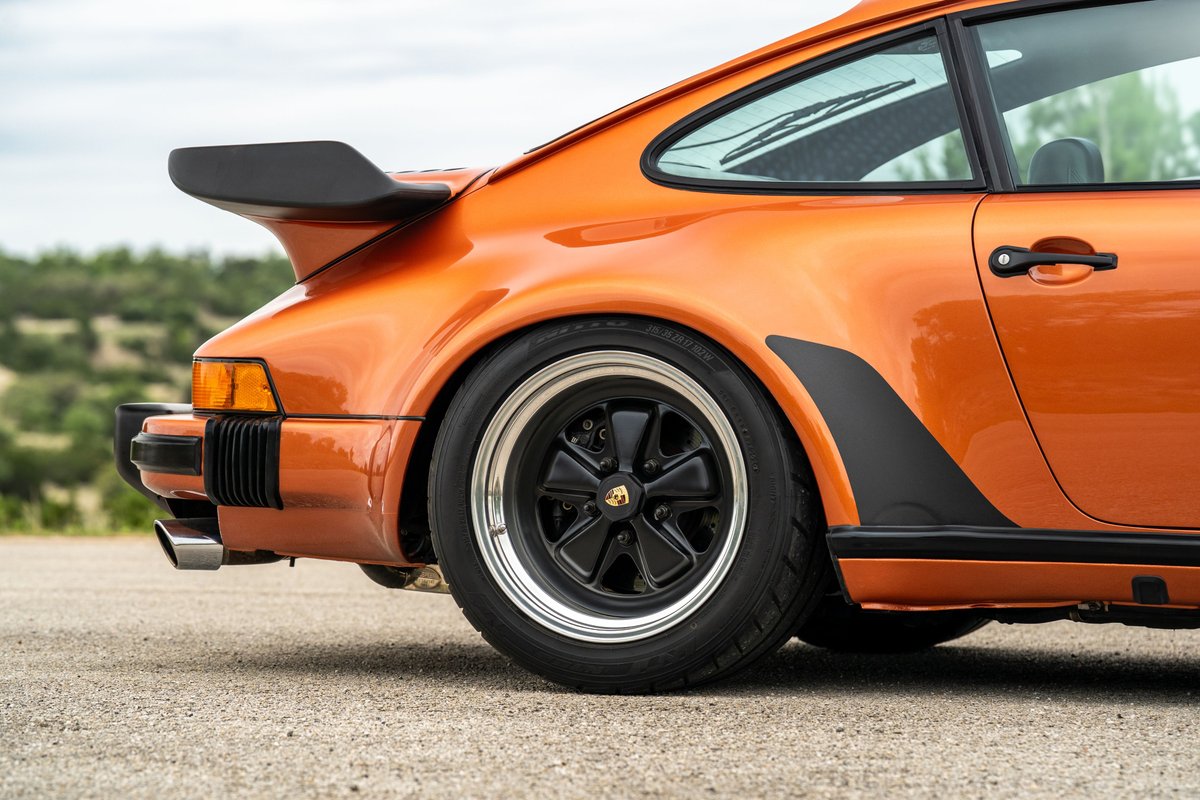 Close-up of an orange metallic 1986 Porsche 930 Turbo rear fender and iconic whale tail spoiler.