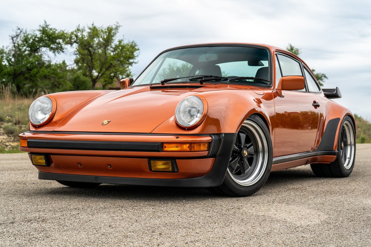 Front 3/4 view of an orange metallic 1986 Porsche 930 Turbo with black trim and Fuchs rims.