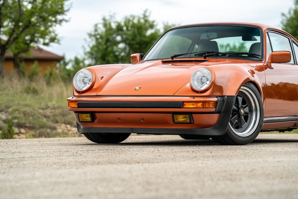 1986 Porsche 930 Turbo in orange metallic, featuring black Fuchs rims.