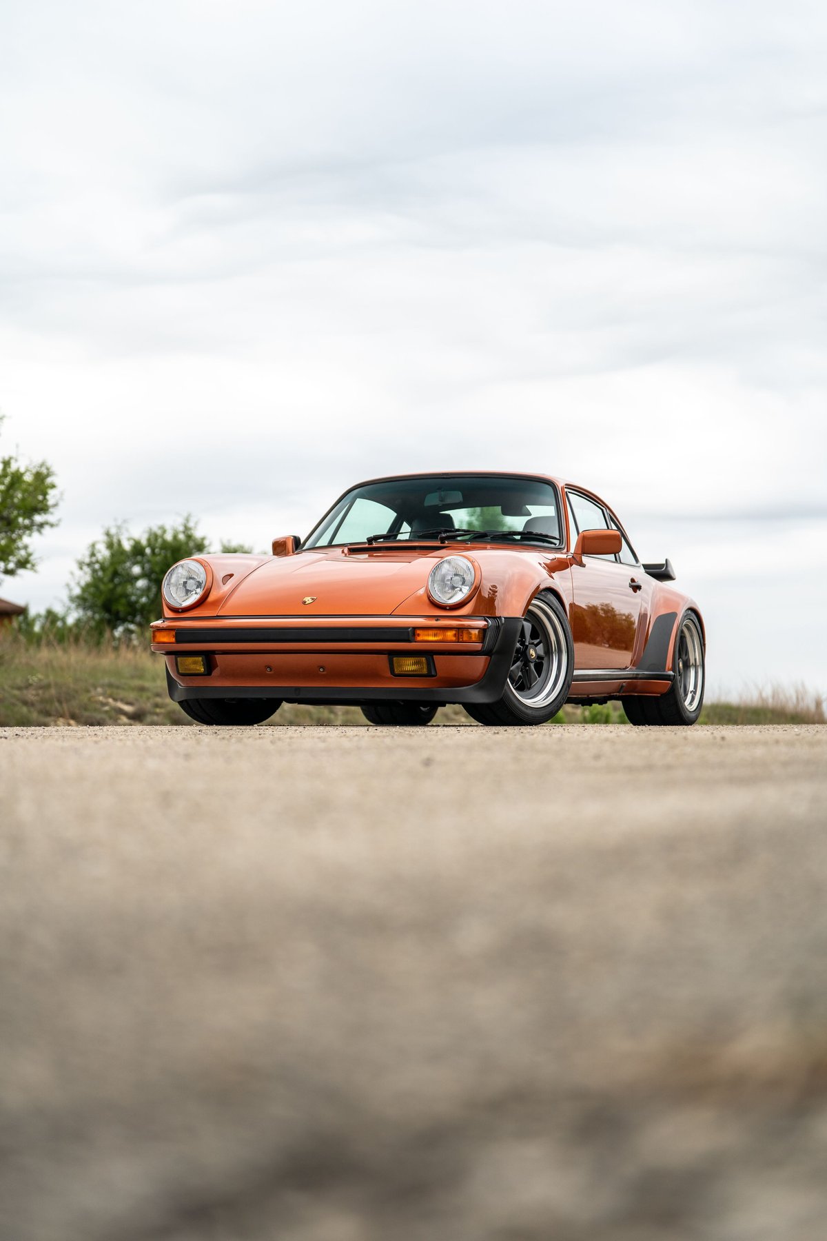 Front view of an orange metallic 1986 Porsche 930 Turbo with black trim and Fuchs rims.