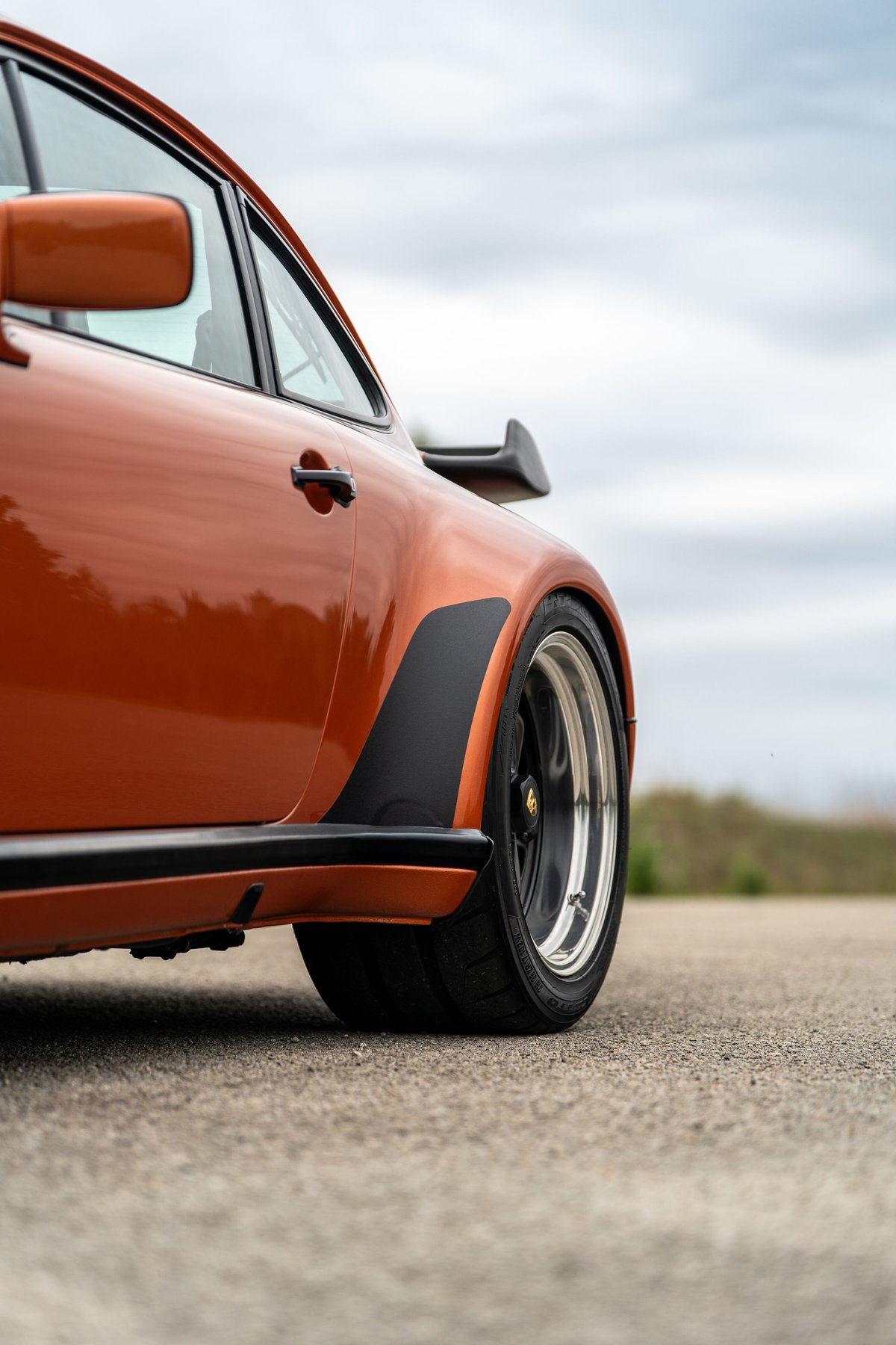 Close up of an orange metallic 1986 Porsche 930 Turbo, showing wide fender flares and chrome lip rims.