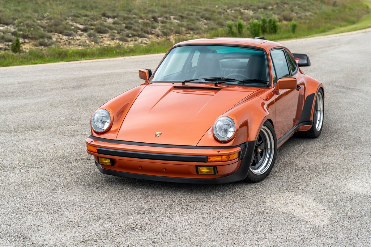 1986 Porsche 930 Turbo in metallic orange, with Fuchs wheels and wide body trim.