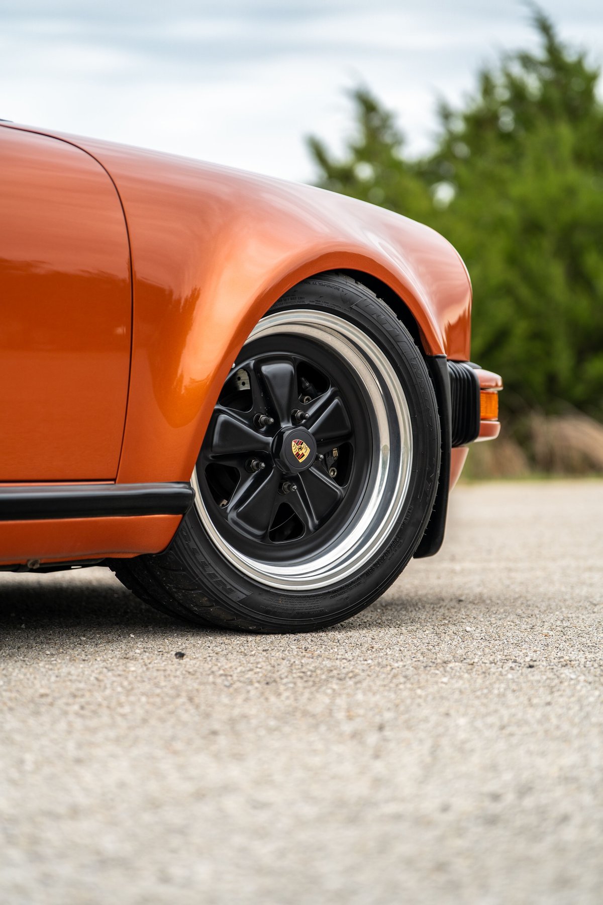 Close-up of an orange metallic 1986 Porsche 930 Turbo front wheel with black Fuchs rims.