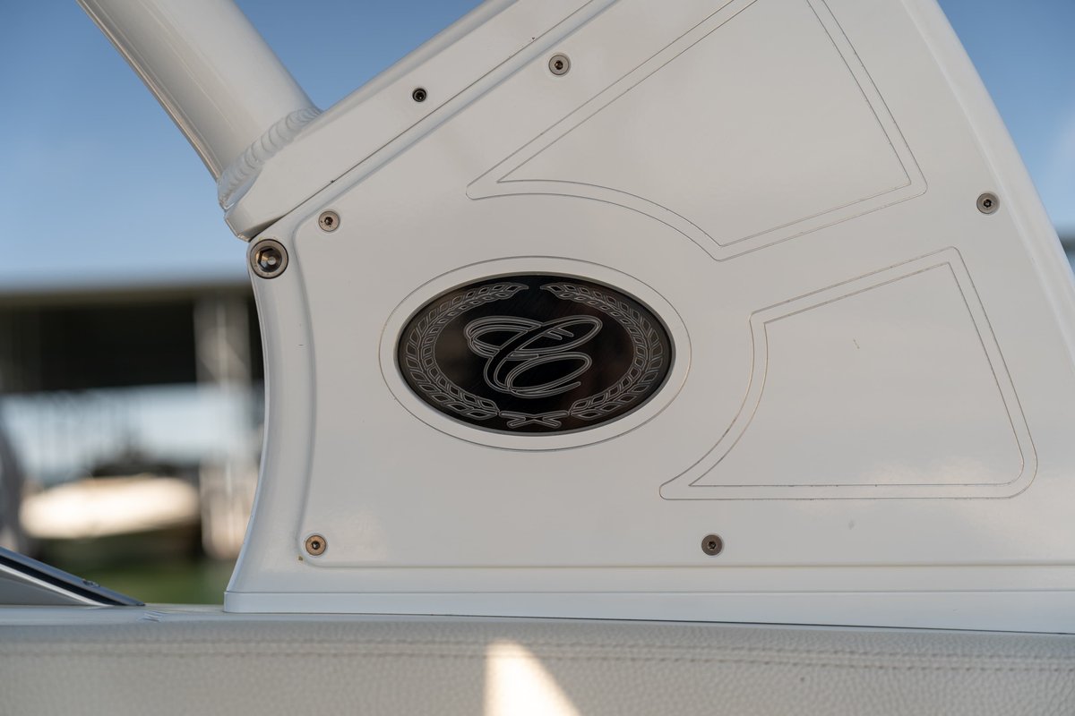 Close-up of a Cobalt R7 Surf boat's white trim featuring an oval emblem with a stylized 'C' logo and laurel wreath.