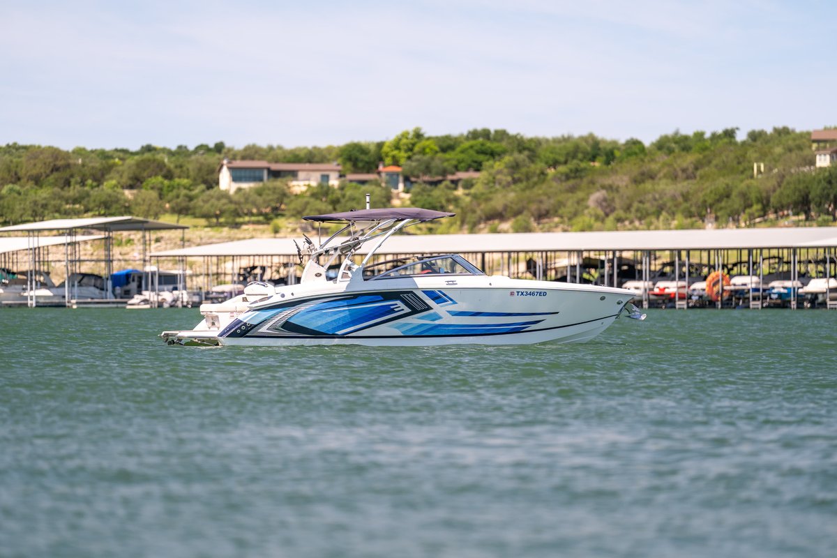 A white Cobalt R7 Surf boat with blue racing livery cruises on a lake.