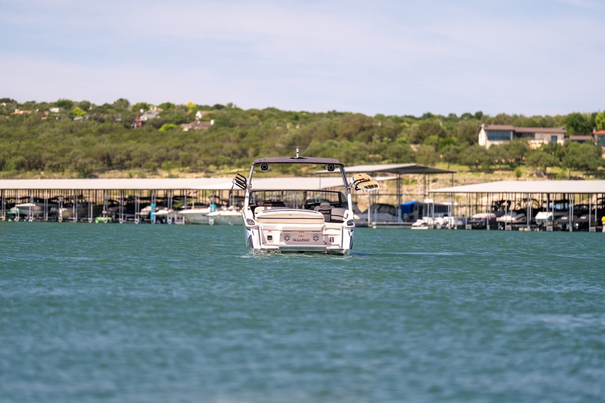 Rear view of a white Cobalt R7 Surf boat, on a lake, with boat docks in the background.