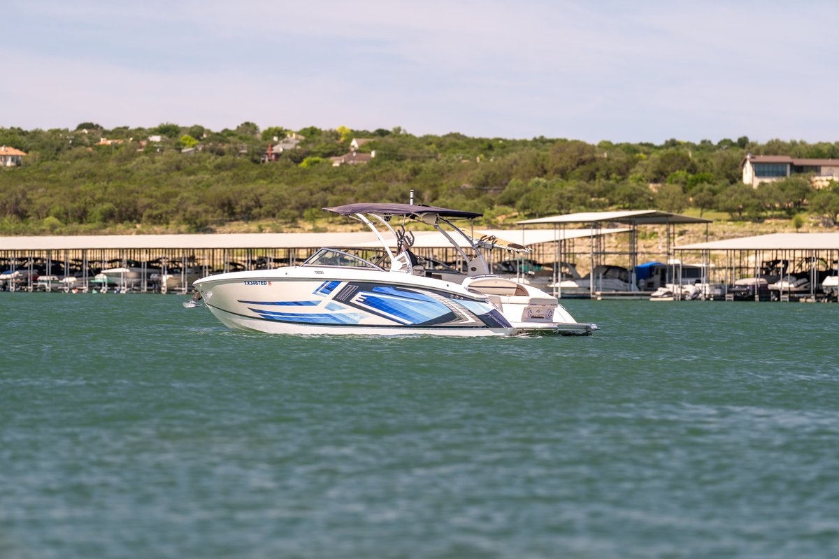 2018 Cobalt R7 Surf boat with blue and silver livery in the water near a marina.