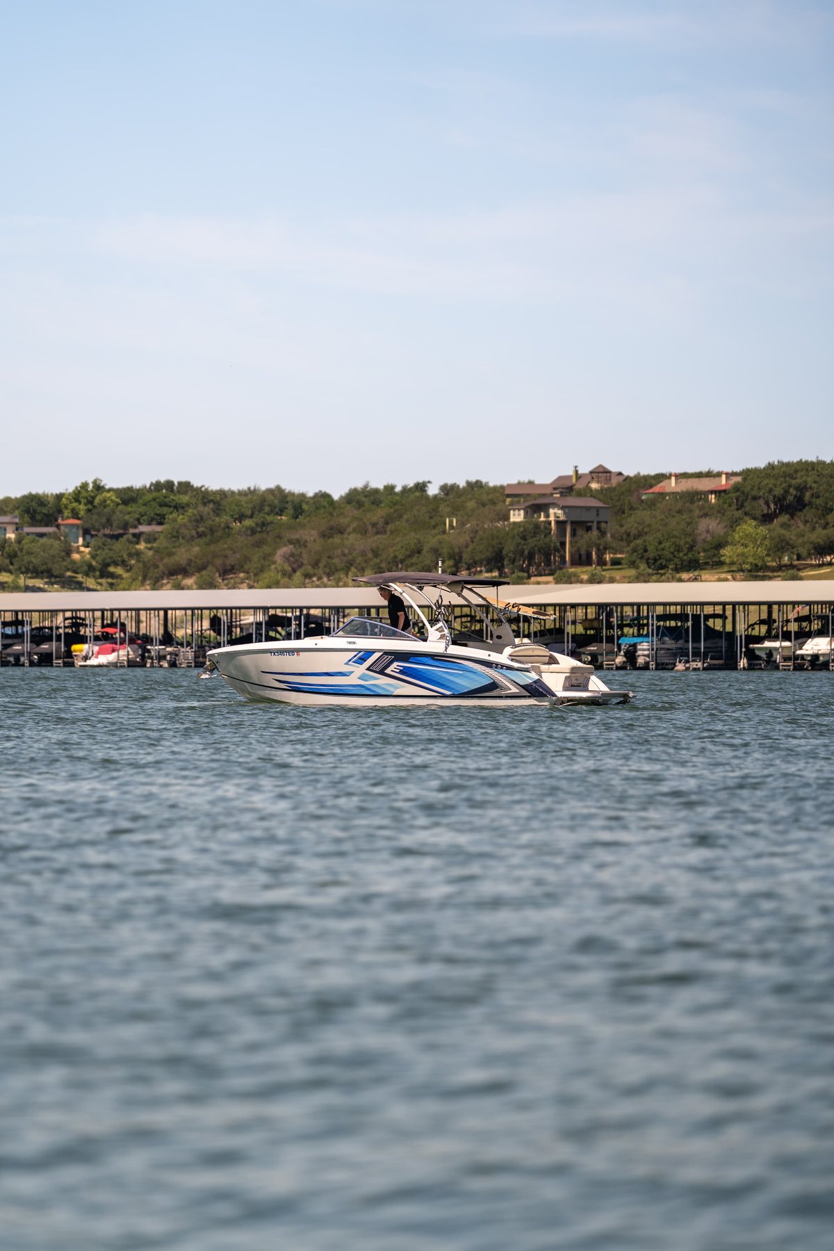 White Cobalt R7 Surf boat with blue and silver livery, docked at a marina on a sunny day.