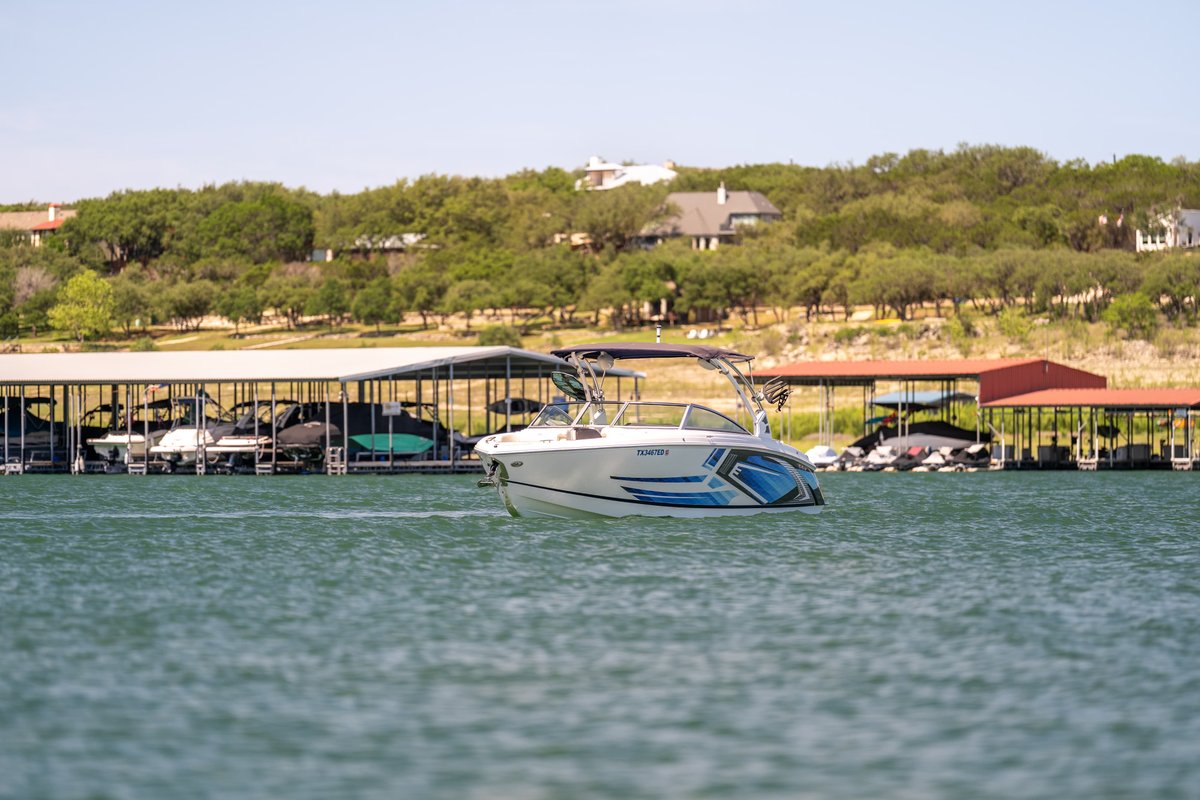 White Cobalt R7 Surf boat with blue graphic livery and bimini top on blue water.