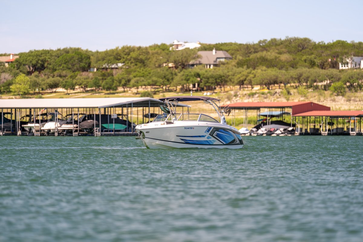 2018 Cobalt R7 Surf boat with blue livery, moving through water near a marina.