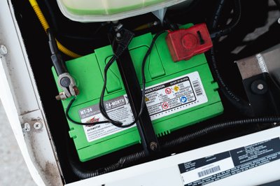 Green automotive battery (MT-34) with terminals and red fuse cover in engine bay of white 1995 Land Rover Range Rover County.