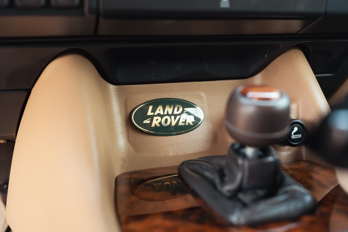 Close-up of the Land Rover logo badge on a tan dashboard trim, next to the gear shifter.