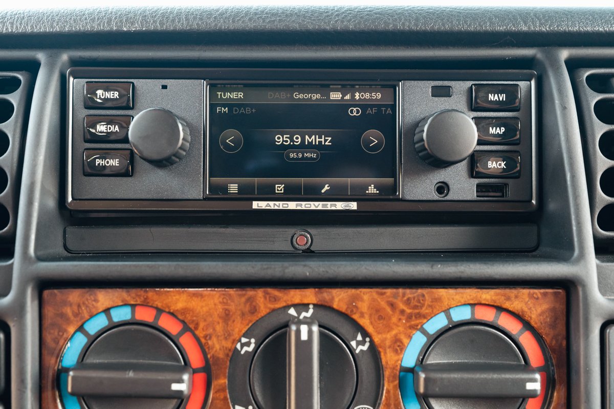 Interior of a white 1995 Land Rover Range Rover County, showing the dashboard infotainment system and climate controls.