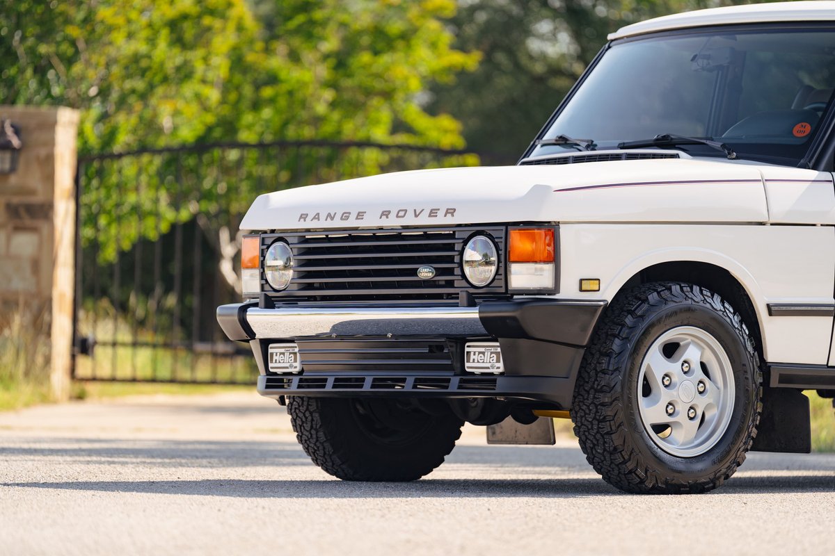 Close-up of a white 1995 Range Rover County with its distinctive grille, round headlights, and classic rims.