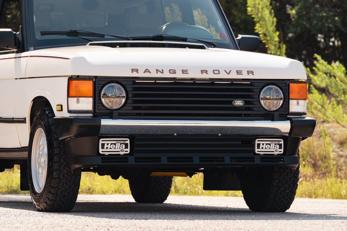 Front view of a white 1995 Range Rover County with chrome grille, Hella fog lights, and chrome five-spoke rims.
