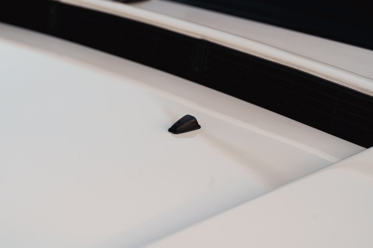 Black windshield washer nozzle on the hood of a white 1995 Land Rover Range Rover County.