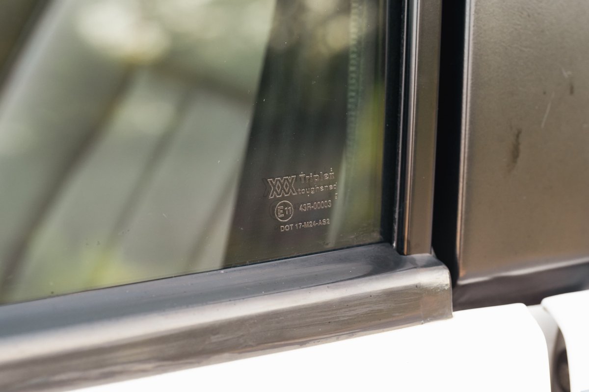 Close-up on the driver's side window of a white 1995 Range Rover County, showing toughened glass markings.