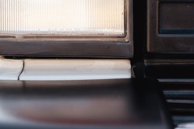 Close-up of a white 1995 Land Rover Range Rover County's headlight trim and dark bumper trim.