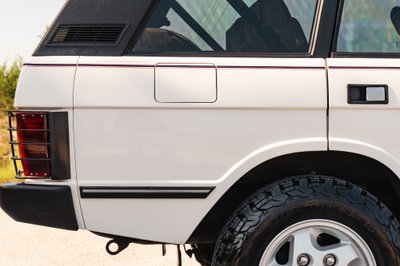 Rear quarter panel of a white 1995 Range Rover County, showing chrome trim, black accents, and alloy rims.