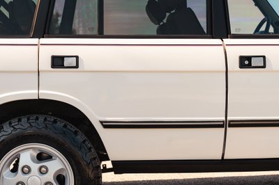 White 1995 Land Rover Range Rover County: detail of door handles, black trim, and alloy rim.