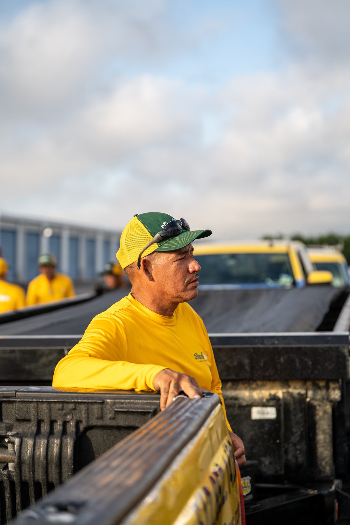 Yellow Grounds Guys Ford F-150 truck, pickup bed, crew cab, with worker in foreground.