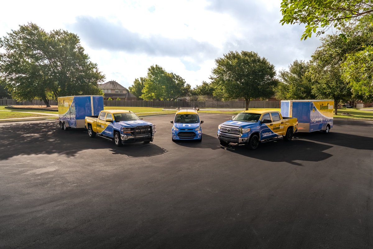 Blue and yellow pickup trucks and a blue car, all with custom livery, parked on asphalt with trailers.