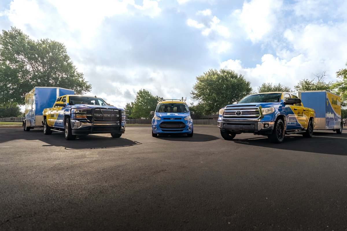 Blue & yellow livery on Chevrolet pickup truck towing a trailer and a Ford Transit Connect van.
