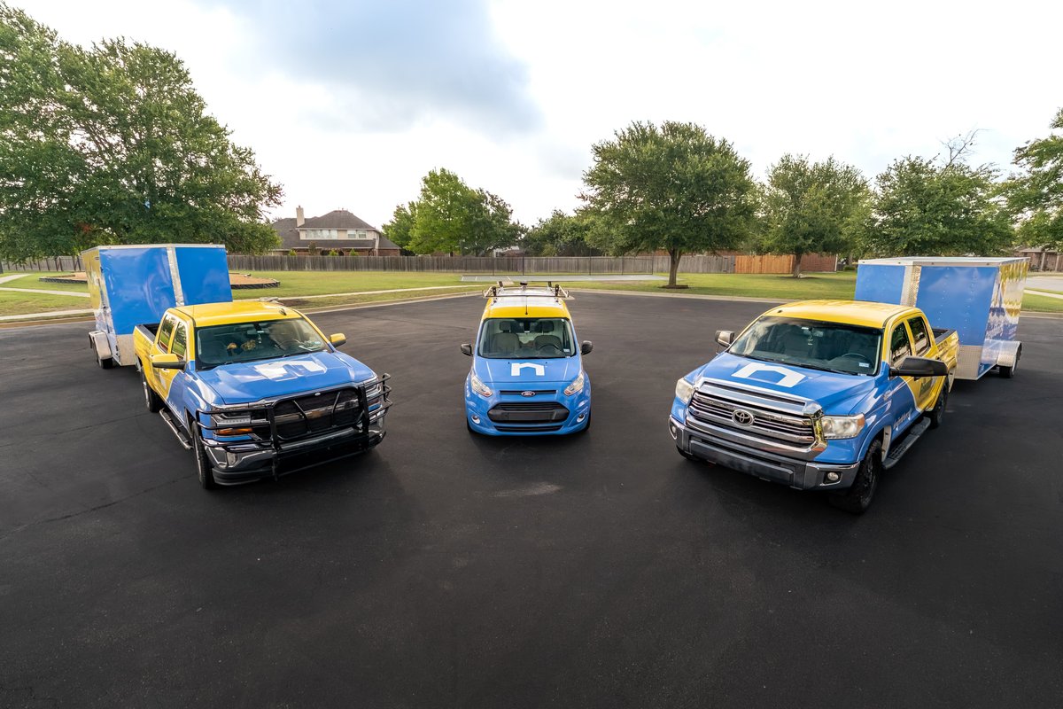 Blue and yellow Toyota Tundra towing a trailer, with other commercial vehicles.