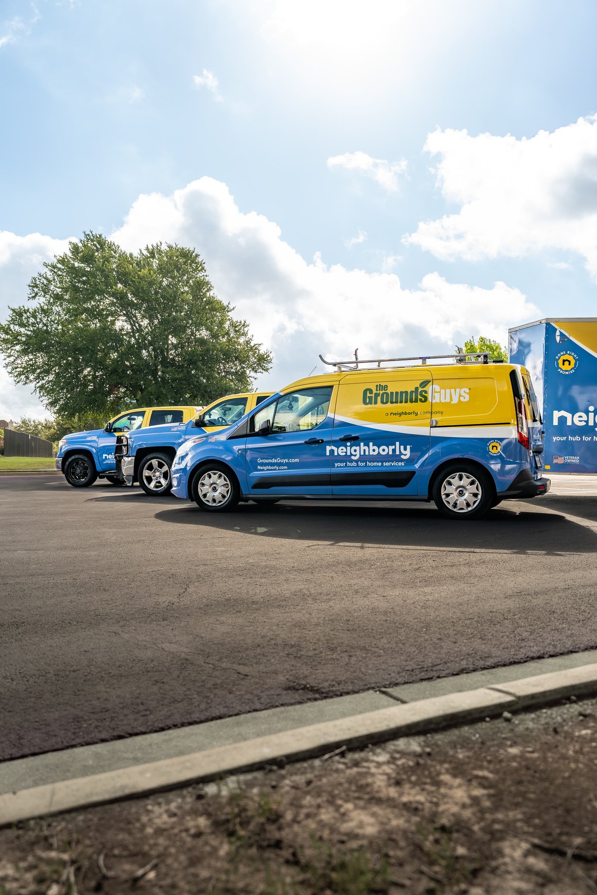 A blue and yellow Ford Transit Connect van with custom livery for "The Grounds Guys" and "Neighborly".
