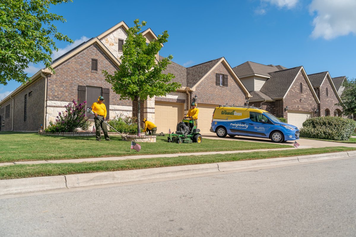 A blue Ford Transit Connect with "Grounds Guys" livery parked in front of a house.