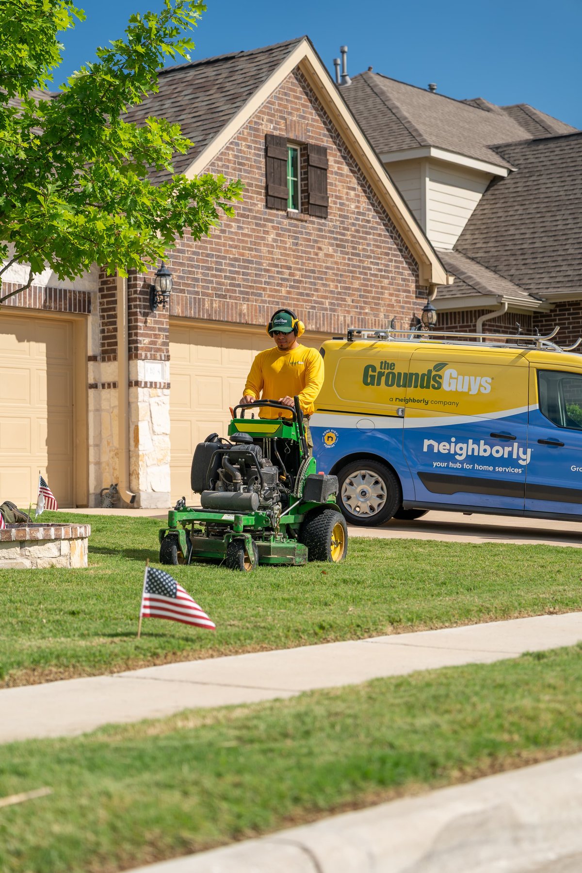 Yellow and blue Neighborly van with "The Ground's Guys" livery, parked beside a lawnmower.