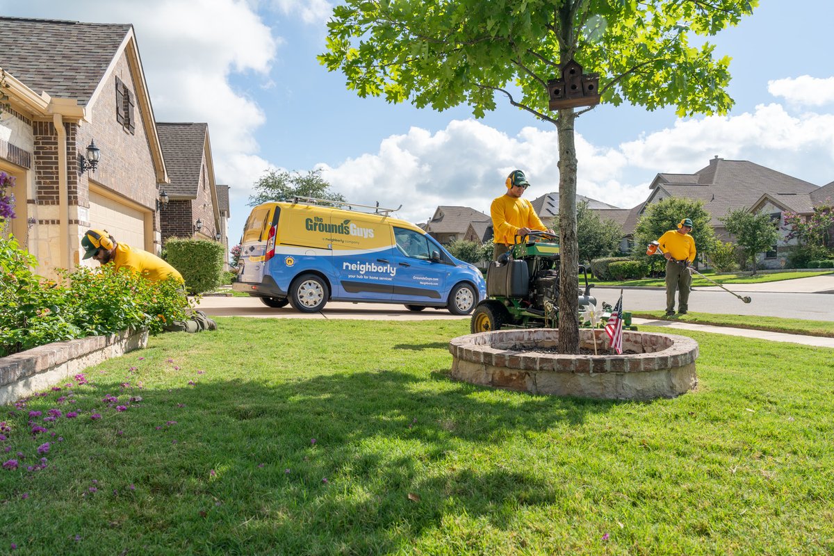 Blue and yellow Ford Transit Connect van with "Grounds Guys" livery, parked in a suburban driveway.