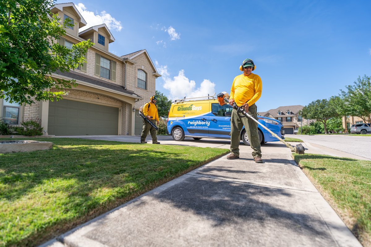 Grounds Guys Neighborly Ford Transit cargo van, blue livery, two workers trim lawn.