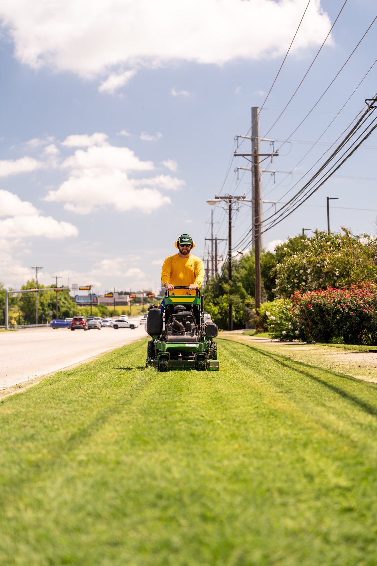 Green John Deere zero-turn mower with a man mowing grass by a roadside.