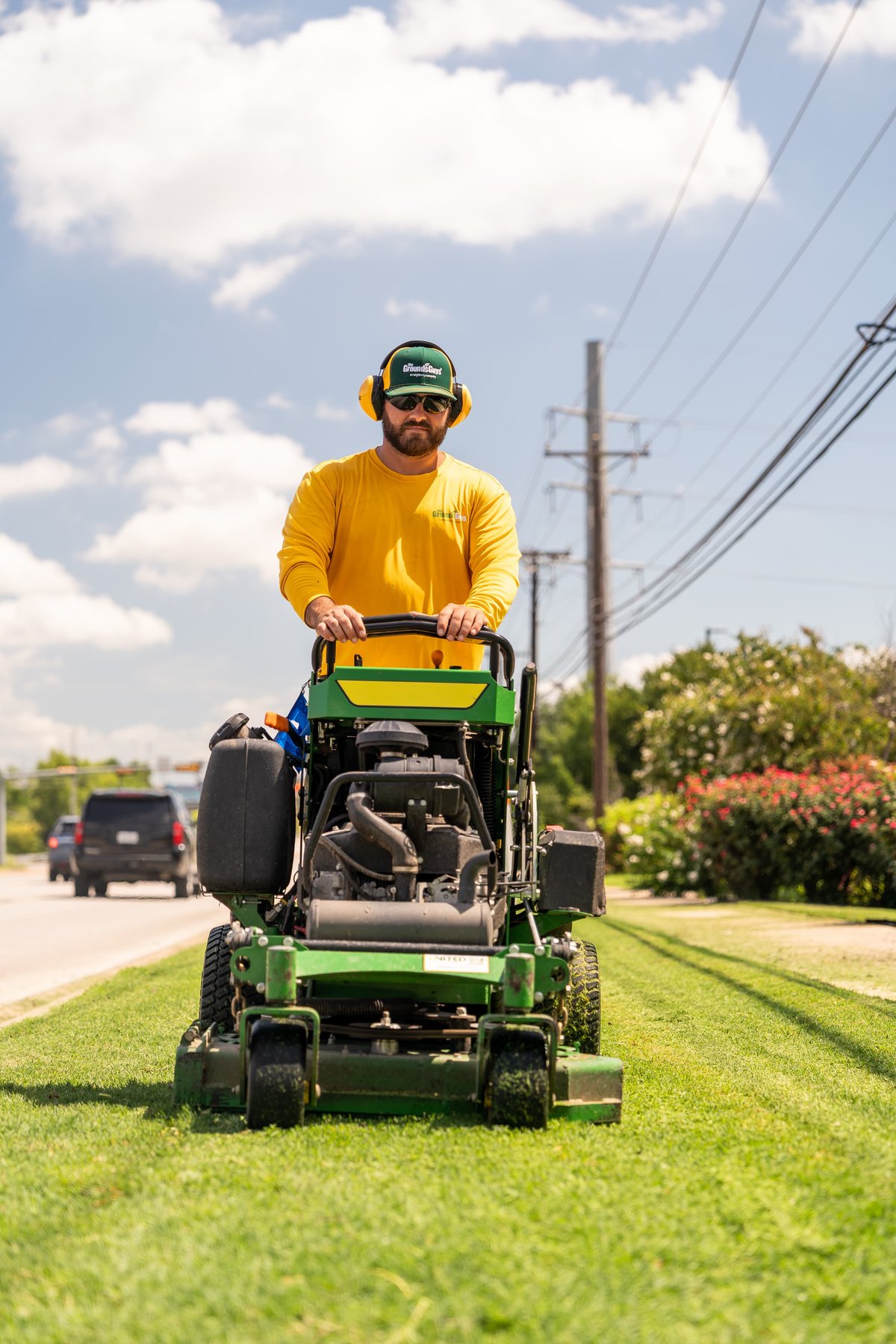 A John Deere commercial zero-turn mower with a man in a yellow shirt and green hat operating it.