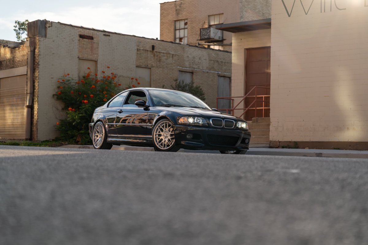 Black 2002 BMW M3 coupe with custom gold rims parked curbside.