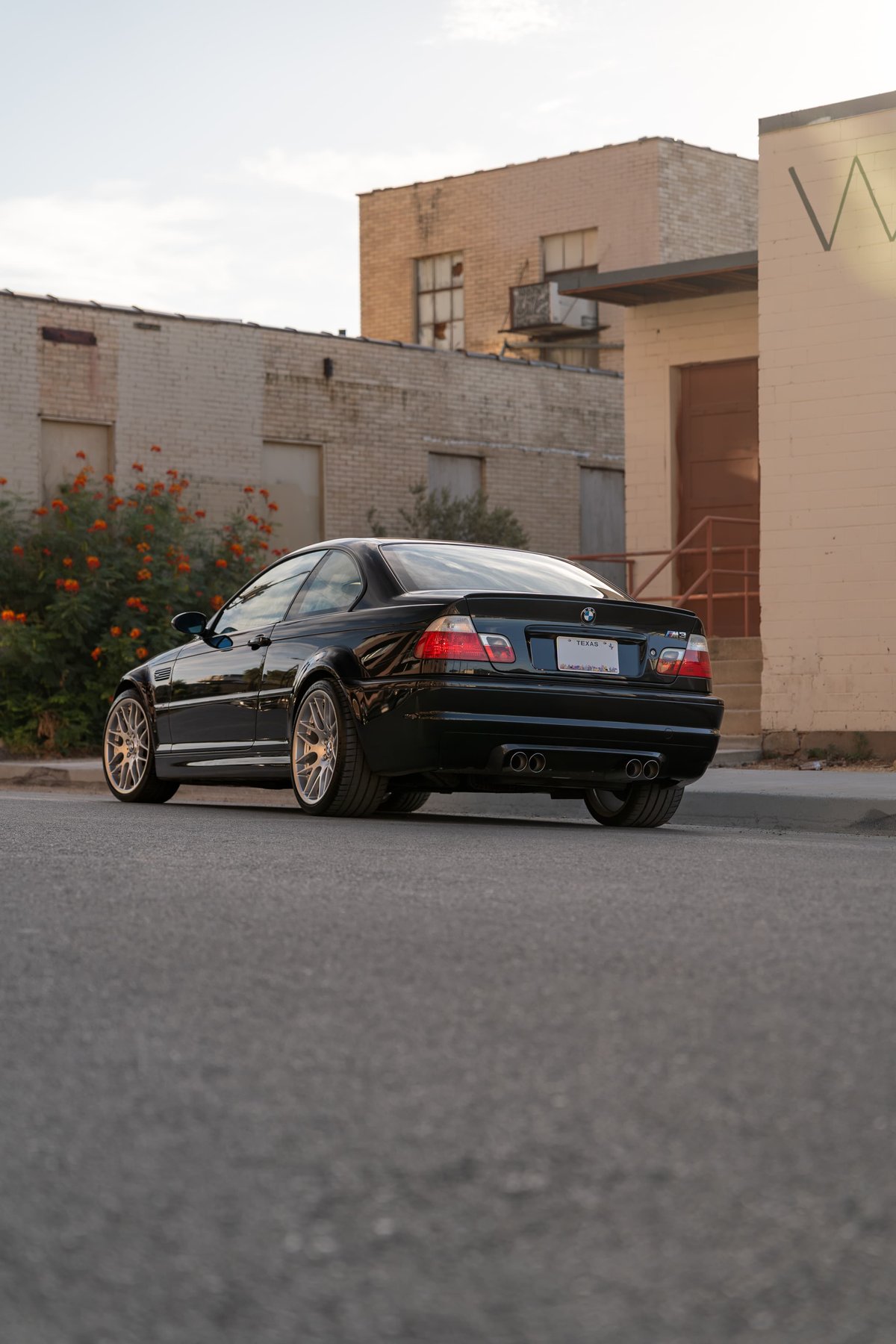 Black 2002 BMW M3 E46 coupe with aftermarket multi-spoke rims and quad exhaust tips.