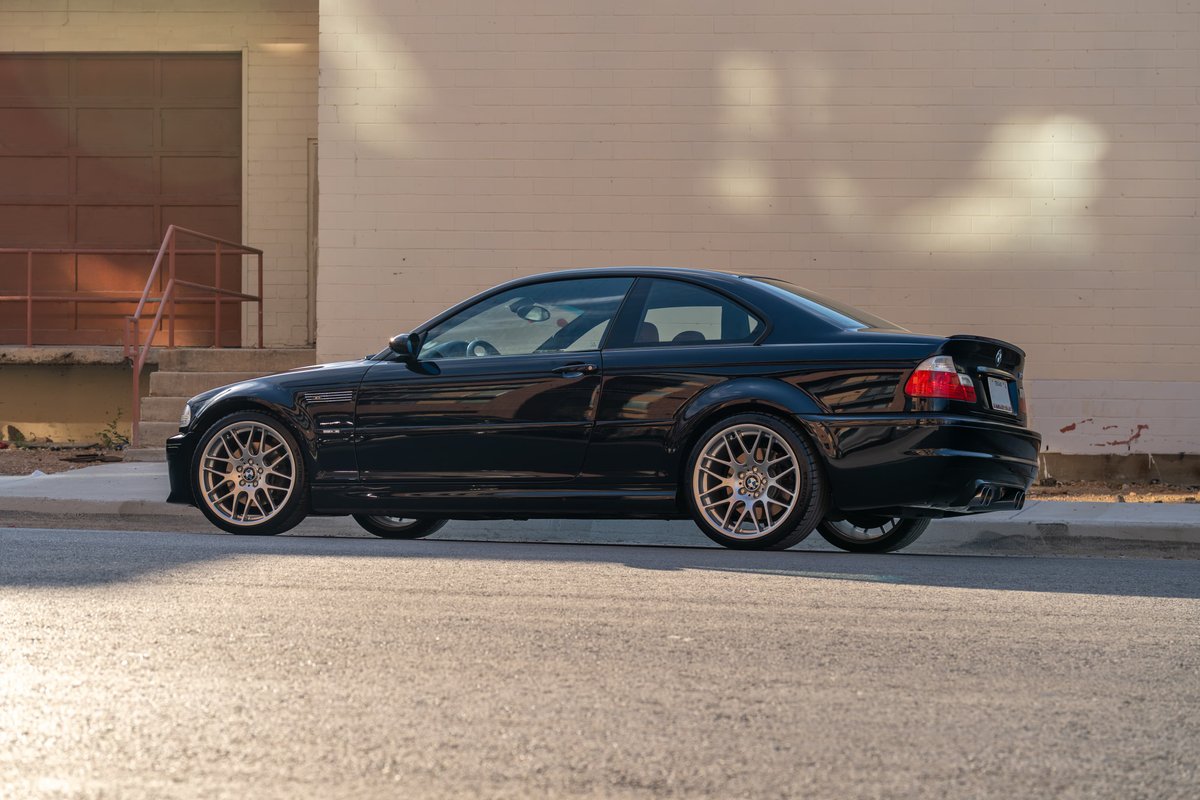 Black 2002 BMW M3 coupe with aftermarket multi-spoke rims and a rear spoiler.